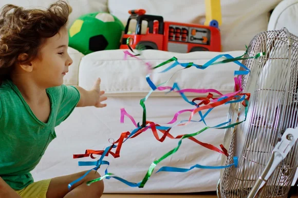 Kind spielt mit Luftschlangen am Ventilator